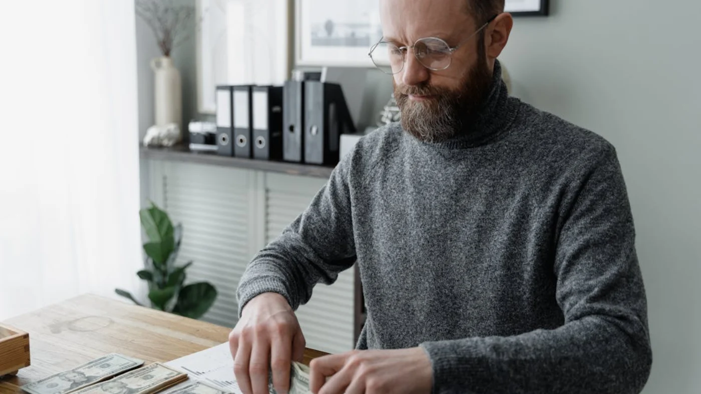 Business owner organizing cash and reviewing documents at desk while setting up payroll for a small business