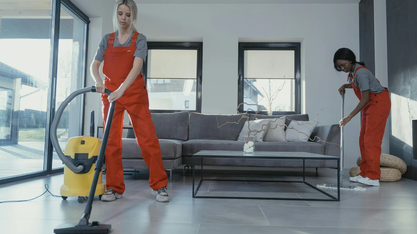 two professional women vacuuming and sweeping a living room