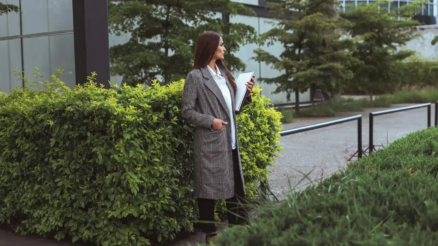 Landscaping business owner reviewing notes outdoors near landscaped property for lawn care proposal planning