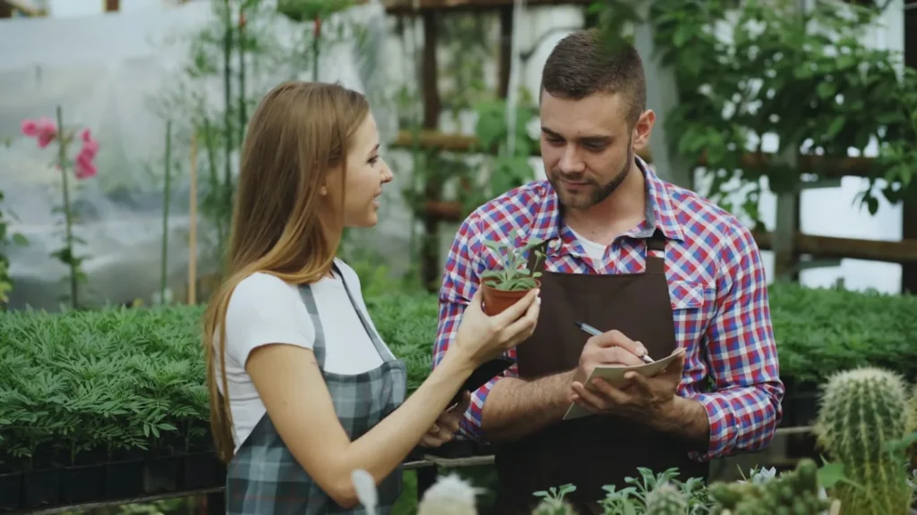Landscaping professional taking notes while discussing a potted plant with a customer, representing writing a lawn care or landscaping invoice