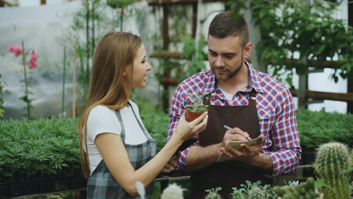 Landscaping professional taking notes while discussing a potted plant with a customer, representing writing a lawn care or landscaping invoice