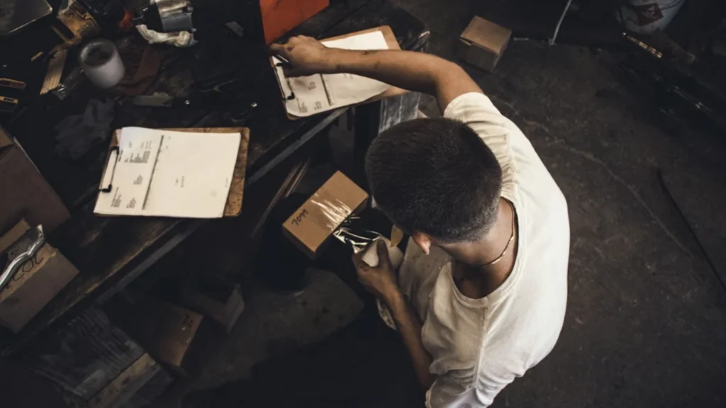 Handyman reviewing paperwork and packaging supplies at a workbench, representing how to write a professional handyman invoice