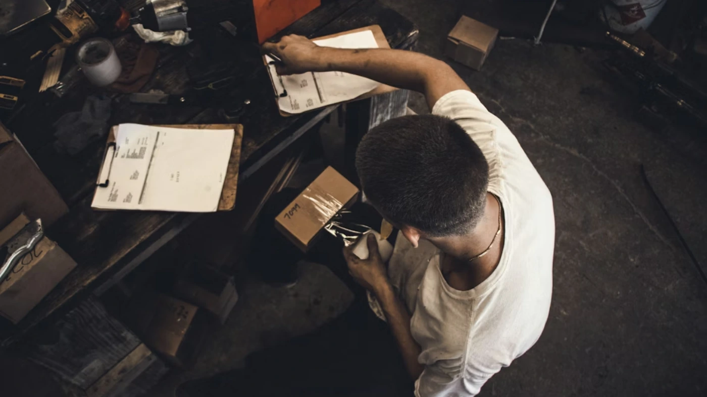 Handyman reviewing paperwork and packaging supplies at a workbench, representing how to write a professional handyman invoice