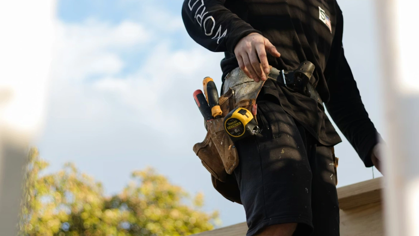 Contractor standing on a roof with tool belt, representing home service professionals using platforms like Angi to find jobs and grow revenue