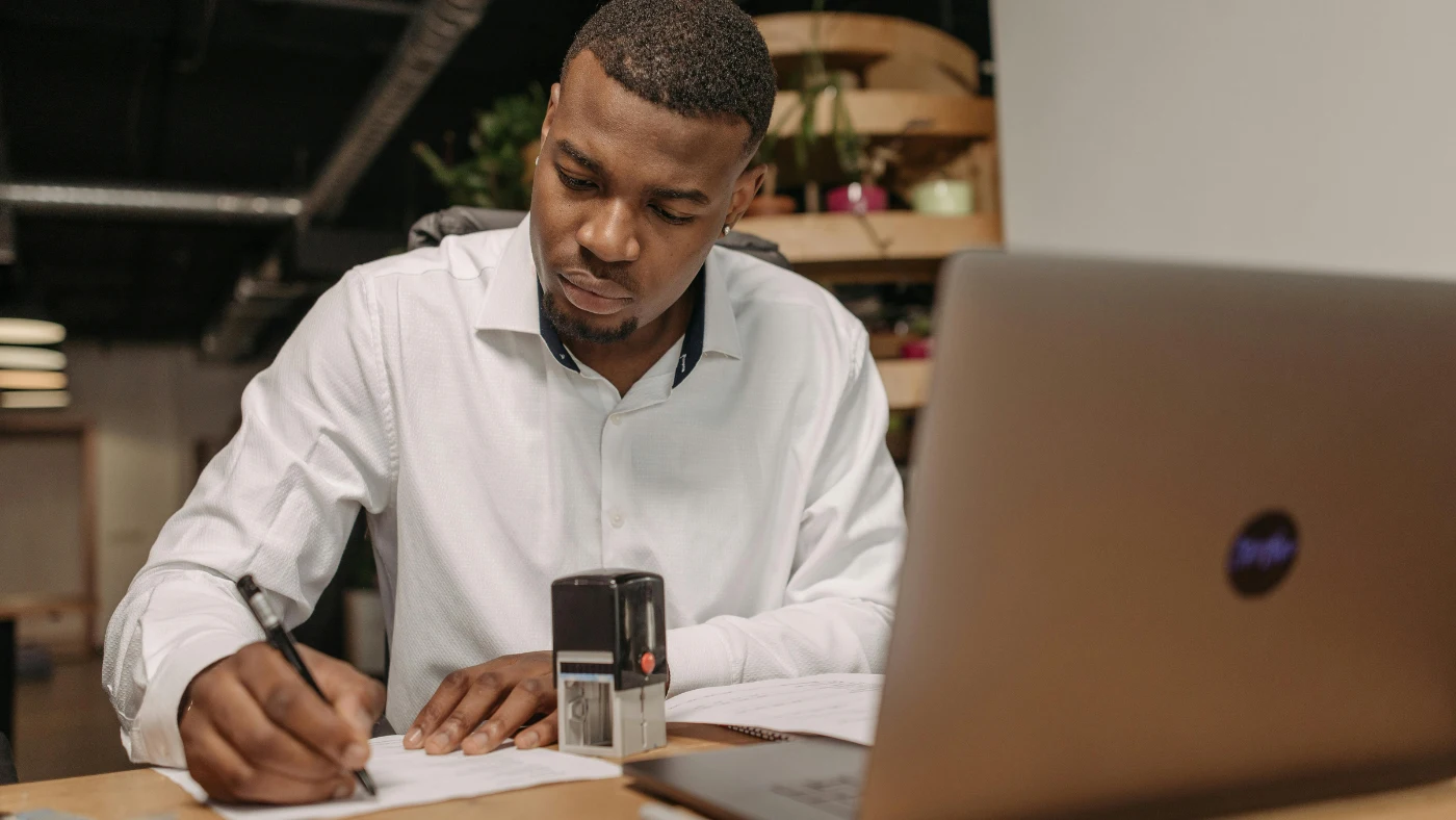 Business owner signing official documents at desk, representing business registration and legal documentation