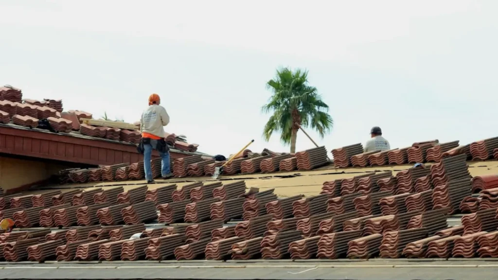 Roofing crew installing clay tiles on residential roof under clear sky