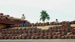 Roofing crew installing clay tiles on residential roof under clear sky