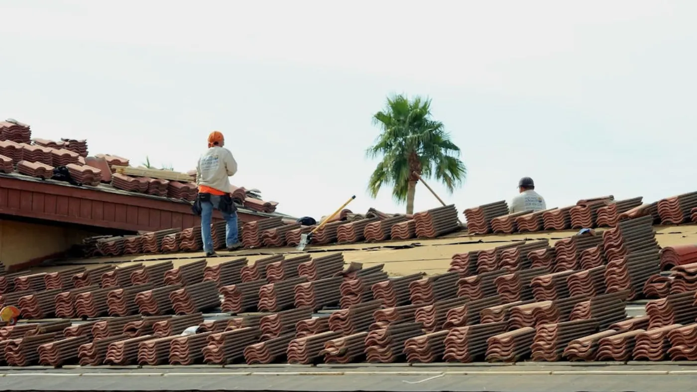 Roofing crew installing clay tiles on residential roof under clear sky