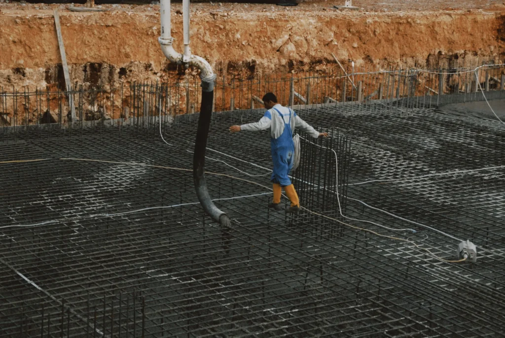 - Housecall Pro Worker walking across a reinforced steel rebar grid used to calculate concrete volume, material costs, and foundation construction pricing.