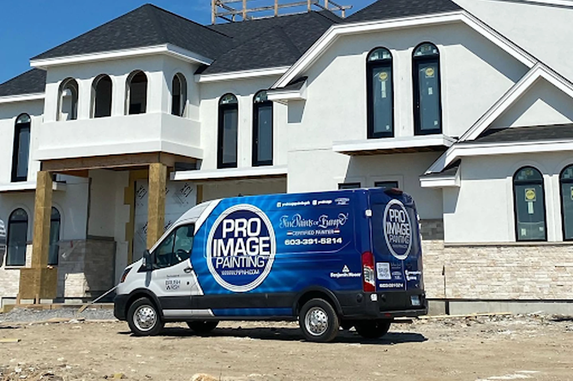 White modern two-story house under construction with arched windows; a blue Pro Image Painting van is parked in front.