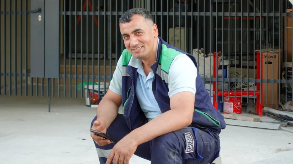Smiling field technician in a work vest holding a smartphone on a job site.