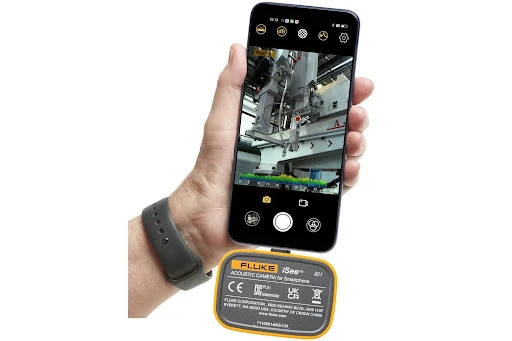 - Housecall Pro Hand with a gray wristband holds a smartphone in camera mode, filming a yellow Fluke device attached to industrial equipment.